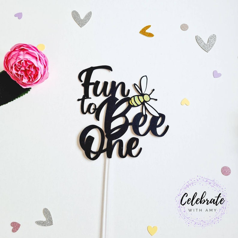 May include: Black cake topper with the text "Fun to Bee One" and a yellow and black bee illustration.