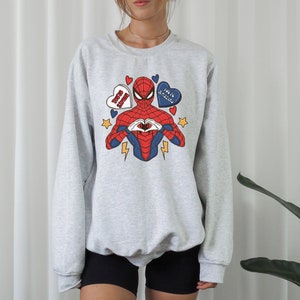 May include: A gray sweatshirt with a graphic print of Spiderman making a heart shape with his hands. The graphic also includes hearts with the text "Love You 3000" and "You're Amazing".