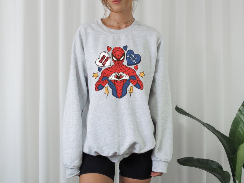 May include: A gray sweatshirt with a graphic print of Spiderman making a heart shape with his hands. The graphic also includes hearts with the text "Love You 3000" and "You're Amazing".