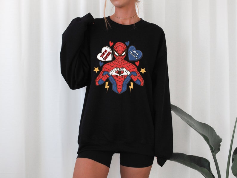 May include: Black sweatshirt with a graphic of Spiderman making a heart shape with his hands. The graphic includes three hearts with the text "You're Amazing", "Be My Boo", and "I Love You" on them.