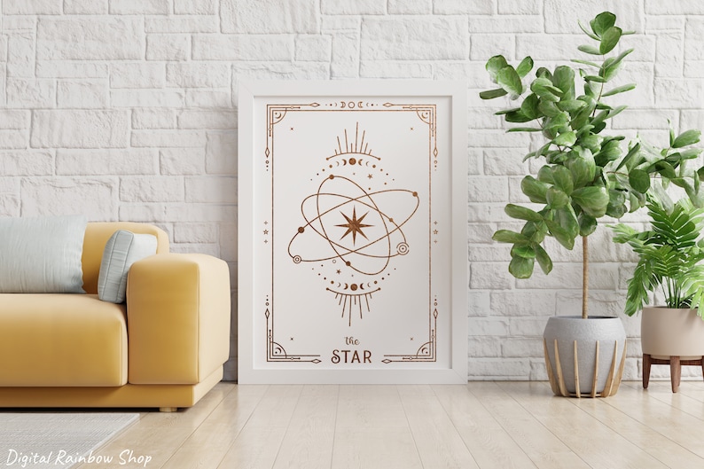 May include: A white framed print with a gold geometric design of a star with a circle around it. The text "The STAR" is at the bottom of the print. The print is hanging on a white brick wall with a green plant in a gray pot to the right.