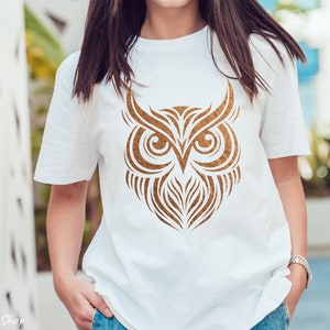 Op de afbeelding: Een wit T-shirt met een gouden uil-ontwerp. De uil is gestileerd met ingewikkelde lijnen en details.