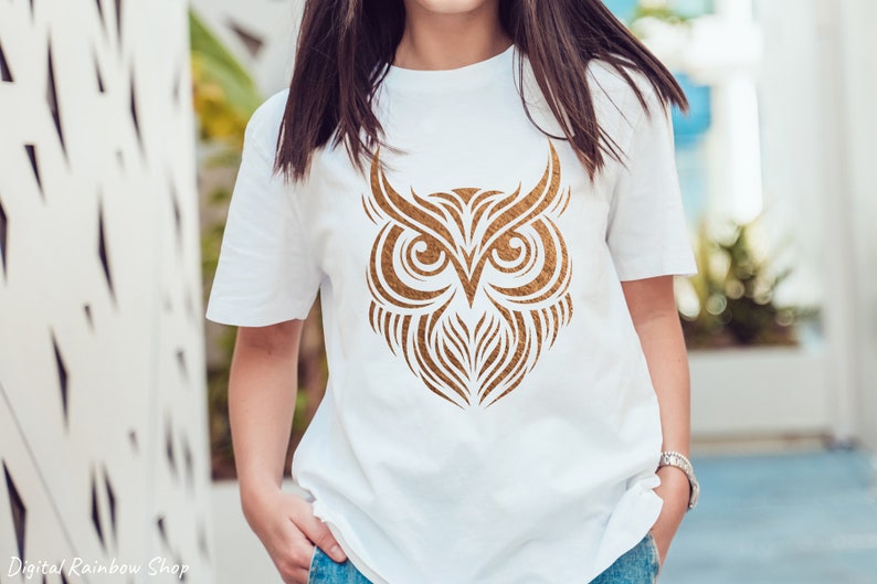 Op de afbeelding: Een wit T-shirt met een gouden uil-ontwerp. De uil is gestileerd met ingewikkelde lijnen en details.