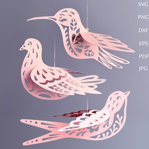 May include: Three-dimensional paper bird mobile in shades of pink. The birds are suspended by strings and feature intricate cut-out designs. The image includes the file type options: SVG, PNG, DXF, EPS, PDF, and JPG.
