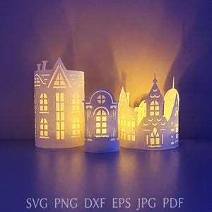 Può includere: Tre lanterne di carta bianca a forma di edifici, ciascuna con finestre e porte ritagliate. Le lanterne sono illuminate dall'interno, creando un bagliore caldo. Il testo "SVG PNG DXF EPS JPG PDF" è in basso.