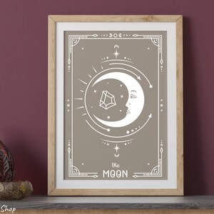 May include: A framed print with a beige background and a white crescent moon with a face. The moon is surrounded by geometric shapes and stars. The text "the MOON" is at the bottom of the print.