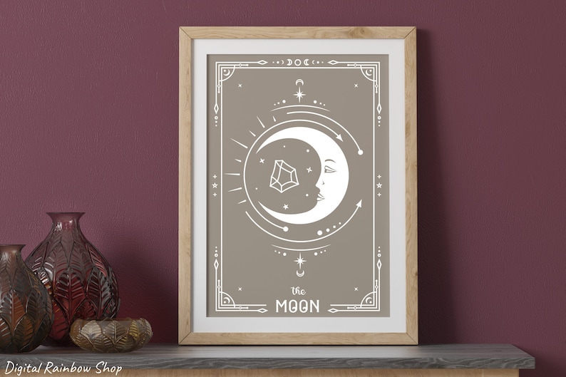 May include: A framed print with a beige background and a white crescent moon with a face. The moon is surrounded by geometric shapes and stars. The text "the MOON" is at the bottom of the print.