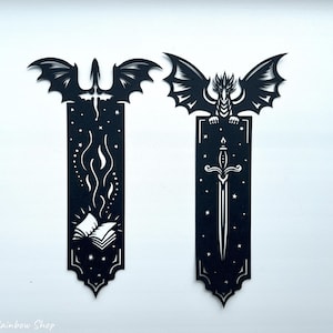 May include: Two black dragon-themed bookmarks. One features a dragon with a sword, the other a dragon with a book and flames. The bookmarks are cut from a dark material and have intricate designs. The text "Digital Rainbow Shop" is at the bottom.