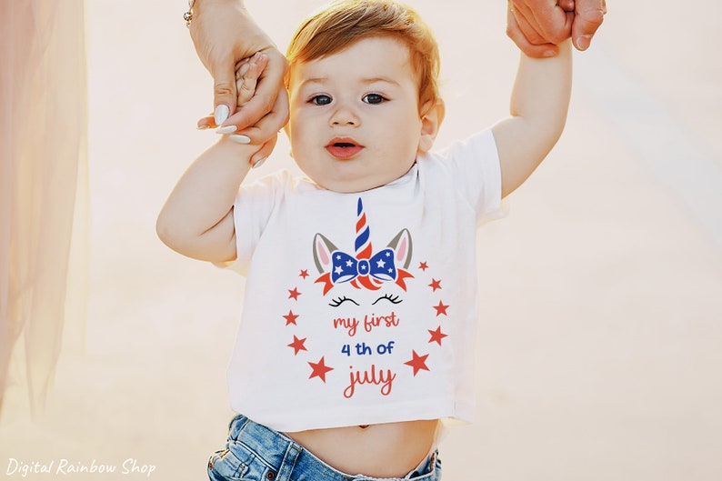 Puede incluir: Una camiseta blanca con un dise&ntilde;o de unicornio rojo, blanco y azul. El unicornio tiene un lazo con estrellas y el texto "my first 4th of july".