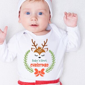 Puede incluir: Un pelele blanco con un lindo dise&ntilde;o de reno y el texto "Baby's First Christmas".