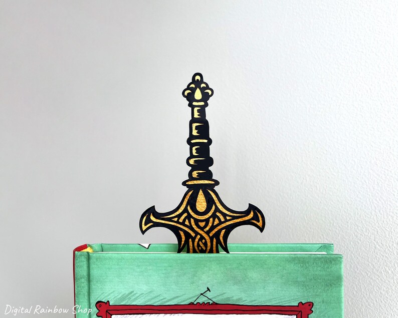 May include: A black and gold sword-shaped bookmark is inserted into a green book. The bookmark has an ornate design with gold accents. The book has a red border and the words "Digital Rainbow Shop" are visible in the bottom left corner.