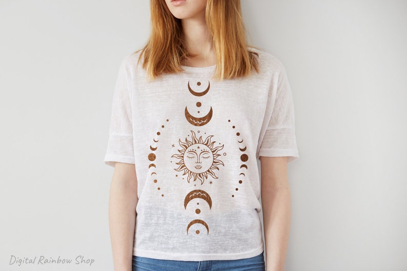 Op de afbeelding: Een wit T-shirt met een bruin zon- en maandesign. De zon heeft een gezicht en de maanfasen zijn in een cirkel eromheen gerangschikt.