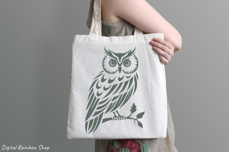Op de afbeelding: Een witte canvas tote bag met een groen uil ontwerp. De uil is gestileerd met een tribale patroon en zit op een tak.
