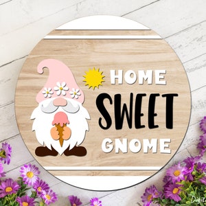 Puede incluir: Un letrero redondo de madera con un gnomo rosa sosteniendo un cono de helado. El letrero dice "Home Sweet Gnome" con un gr&aacute;fico de sol amarillo.