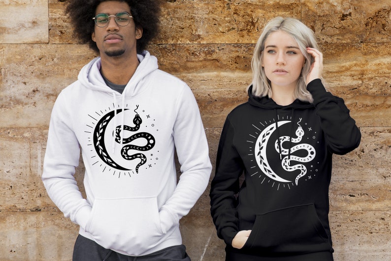 Op de afbeelding: Twee mensen dragen zwarte en witte hoodies met een afbeelding van een slang die om een halve maan gewikkeld is. De afbeelding is in zwart en wit en heeft een hemels thema.