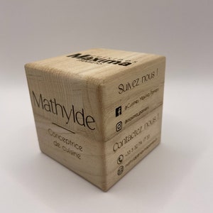 Peut inclure: Un cube en bois avec le texte "Mathylde Conceptrice de cuisine" sur un côté et "Maxima Cuisines" et les coordonnées sur l'autre côté.