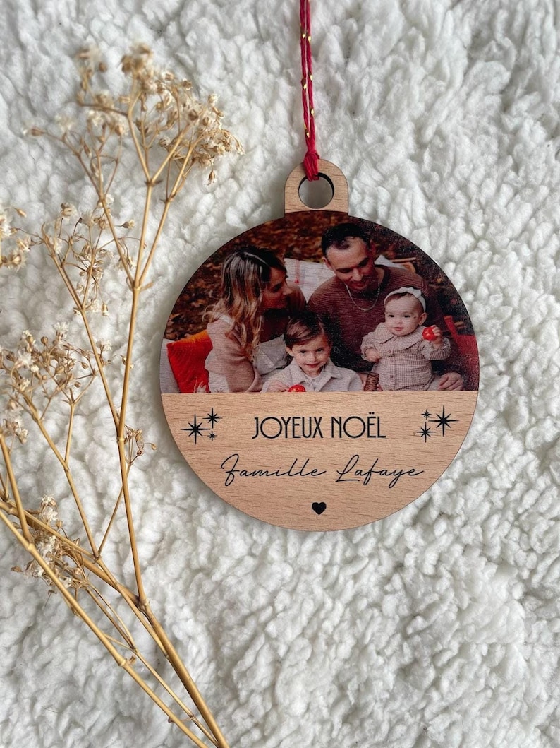 May include: A round wooden Christmas ornament with a photo of a family of four. The ornament is decorated with the text "Joyeux No&euml;l" and "Famille Lafayette" with a small heart.