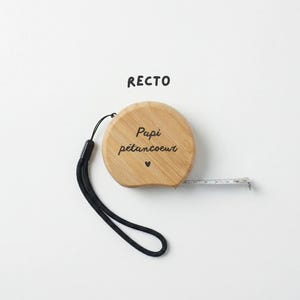 Peut inclure: Un m&egrave;tre ruban en bois avec l'inscription "Papi p&eacute;tancoeur" et un petit symbole de c&oelig;ur. Le ruban a une dragonne noire et un ruban &agrave; mesurer blanc qui s'&eacute;tend du bo&icirc;tier en bois. Le mot "RECTO" est imprim&eacute; au-dessus du ruban.
