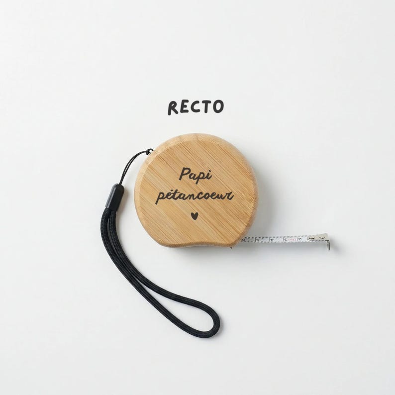 Peut inclure: Un m&egrave;tre ruban en bois avec l'inscription "Papi p&eacute;tancoeur" et un petit symbole de c&oelig;ur. Le ruban a une dragonne noire et un ruban &agrave; mesurer blanc qui s'&eacute;tend du bo&icirc;tier en bois. Le mot "RECTO" est imprim&eacute; au-dessus du ruban.