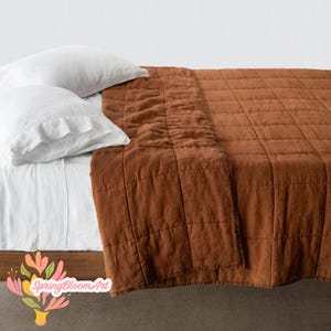 May include: A bedding set featuring a rust-colored quilted coverlet with a grid-stitched pattern and two white pillowcases. The coverlet has a textured appearance and covers the bed, while the white pillows are placed at the head of the bed.