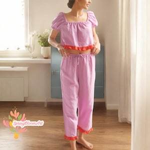 Könnte beinhalten: Ein zweitteiliger Schlafanzug in Lavendelfarbe mit einem kurzen Oberteil und einer Hose. Das Oberteil hat einen quadratischen Ausschnitt und Puffärmel. Sowohl das Oberteil als auch die Hose haben einen roten Rüschenbesatz.