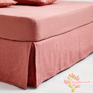 May include: A bed with a dusty rose linen fitted sheet and bed skirt. The bed skirt has a pleated design. Two pillows are visible at the top of the bed. The bedding is made of a soft, textured fabric.