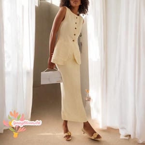 Può includere: Una donna indossa un abito di lino giallo chiaro senza maniche con gonna e top abbinato. Il top ha una chiusura con bottoni sul davanti e una tasca sul lato sinistro. Porta una borsa bianca e sandali dorati.