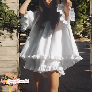 May include: A white, ruffled dress with short sleeves and a tiered skirt. The dress has a loose, flowing silhouette and is made of a lightweight fabric. The image also includes the text "SpringBloomArt" in the lower left corner.