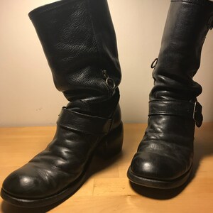 May include: A pair of black leather motorcycle boots with buckles and zippers. The boots have a slightly distressed look and are worn.