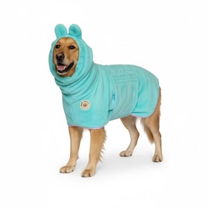 May include: A golden retriever wearing a light blue dog robe with a hood and ear-shaped accents. The robe has a pocket and a light purple trim. A circular patch with text is on the robe. The dog is standing on a white background.