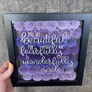Puede incluir: Una caja de sombra enmarcada en negro con un degradado de flores de papel morado y blanco. El texto dentro de la caja dice "You are beautiful for you are fearfully & wonderfully made."