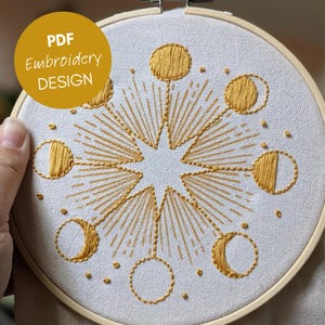 Peut inclure: Broderie sur tambour avec un motif céleste doré, comprenant une étoile centrale et des lunes. Le texte "PDF Embroidery DESIGN" est dans un cercle jaune. Le motif est sur un tissu blanc.