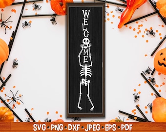Może przedstawiać: Czarny drewniany znak z białym szkieletem trzymającym litery "WELCOME" przed sobą. Znak jest otoczony pomarańczowymi i czarnymi dekoracjami halloweenowymi.