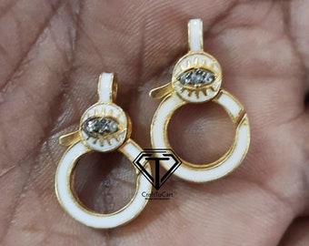 May include: Two gold-colored, eye-shaped clasps with white enamel and small, gray gemstones. The clasps are open, with a circular design and a small loop at the top. The clasps are likely for jewelry or other small accessories.