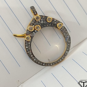 Könnte beinhalten: Ein goldfarbener und schwarzer Metallverschluss mit einem runden Design und kleinen Diamanten. Der Verschluss ist für die Schmuckherstellung gedacht.