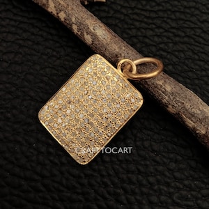 May include: A gold pendant with a square shape, completely covered in small, white diamonds. The pendant has a loop at the top for attaching to a chain.