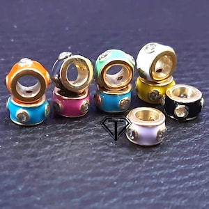 Puede incluir: Ocho abalorios de cuentas de esmalte de colores y tono dorado con diamantes de imitación transparentes. Las cuentas son de color turquesa, rosa, negro, amarillo, verde, naranja y lavanda.