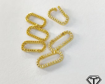 May include: Gold-colored oval-shaped jewelry clasps with clear, sparkling stones set along the edges. Several clasps are open, while others are closed. The clasps are scattered on a white surface.