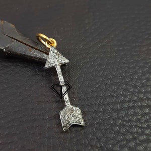 Può includere: Un ciondolo a forma di freccia in argento con un'anellina in oro, incastonato con piccoli diamanti bianchi. La freccia punta verso l'alto.