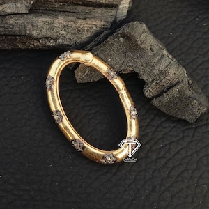 Puede incluir: Anillo de metal de forma ovalada en tono dorado con un diseño decorativo de pequeñas piedras negras. El anillo está abierto por un lado y tiene un cierre de resorte.