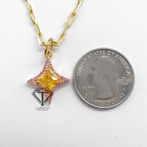 May include: A gold chain necklace with a pendant featuring a yellow gemstone surrounded by pink gemstones in the shape of a four-pointed star. The pendant is about the size of a US quarter.