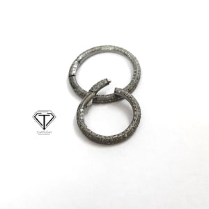 May include: Two silver hoop earrings with a pave diamond setting. The earrings are made of metal and have a shiny finish.