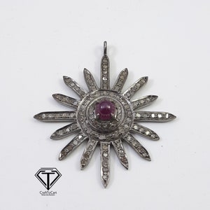 May include: A silver pendant in the shape of a sun with a red gemstone in the center and small diamonds around the edges.