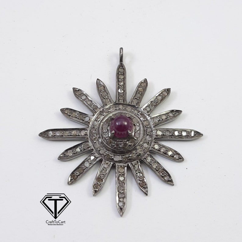 May include: A silver pendant in the shape of a sun with a red gemstone in the center and small diamonds around the edges.