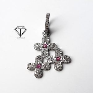 May include: Silver pendant with three interconnected flower designs, each with a small red gemstone in the center and set with small diamonds.