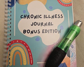 May include: A blue and green journal with the title "Chronic Illness Journal Bonus Edition" and a rainbow design. A black and green pen is lying on top of the journal.