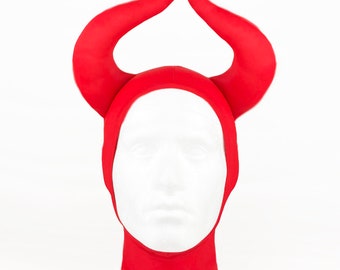 May include: Red devil horns headwear with a red fabric hood. The horns are made of a soft, plush material.