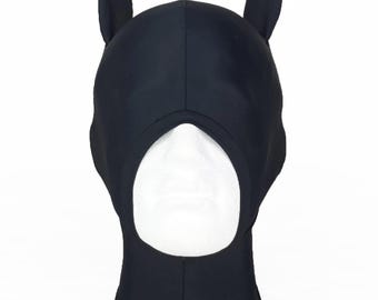 May include: Black hood with attached upright ears, designed to cover the head and neck. The hood has a large oval opening for the face. The ears are rounded and stand up straight. The hood is made of a smooth, opaque material.