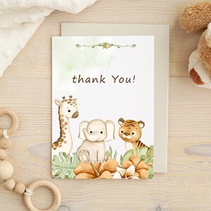 May include: A thank you card with a watercolor illustration of a giraffe, elephant, and tiger surrounded by green leaves and orange flowers. The text "thank you!" is printed in black.