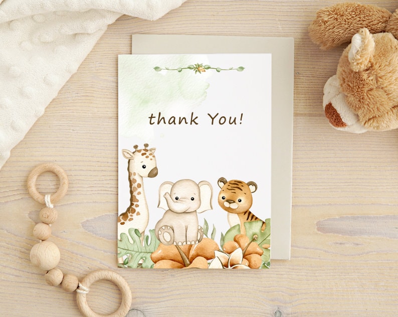 May include: A thank you card with a watercolor illustration of a giraffe, elephant, and tiger surrounded by green leaves and orange flowers. The text "thank you!" is printed in black.